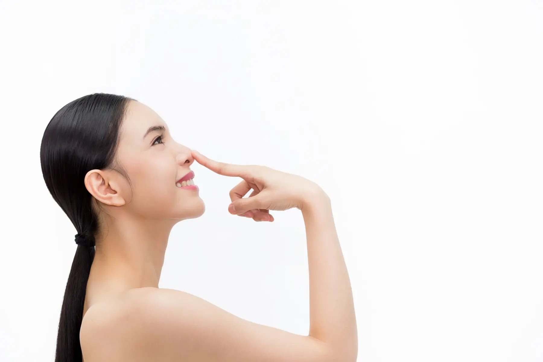 Woman smiling, touching her nose, on white background.